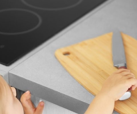 Child reaching for a sharp kitchen knife on counter, illustrating lack of nanny safety awareness and supervision.