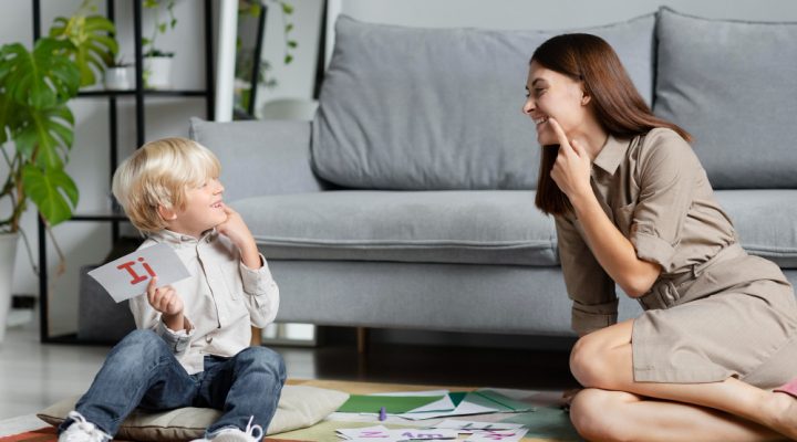 Nanny teaching a smiling child letters on the floor – Power-Nanny educational development blog.